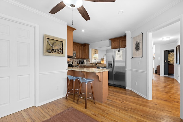 kitchen featuring light wood-type flooring, a kitchen bar, stainless steel appliances, ceiling fan, and light stone countertops