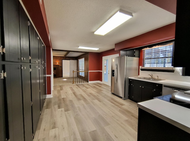 kitchen with stainless steel refrigerator with ice dispenser, sink, a textured ceiling, and light wood-type flooring