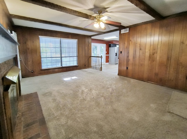 unfurnished living room with a brick fireplace, beam ceiling, wooden walls, and a wealth of natural light