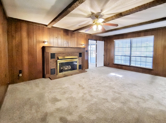 unfurnished living room with a brick fireplace, beam ceiling, wooden walls, and carpet flooring