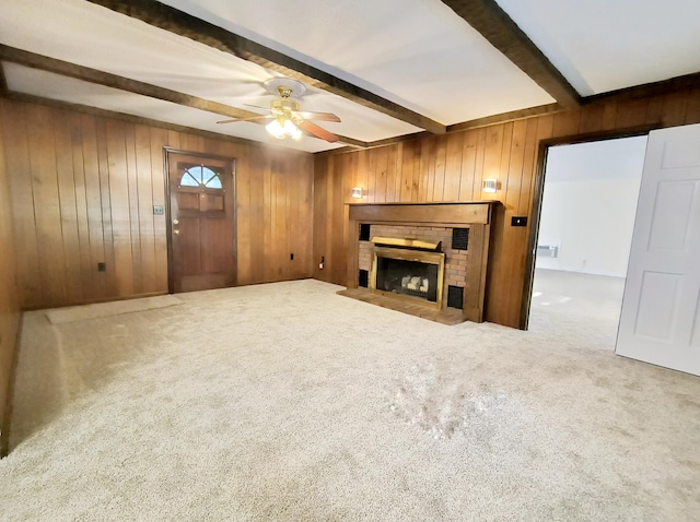 carpeted living room featuring ceiling fan, beam ceiling, a brick fireplace, and wood walls