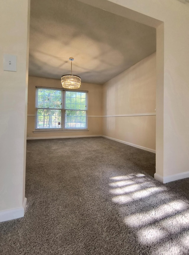 empty room with an inviting chandelier and dark colored carpet