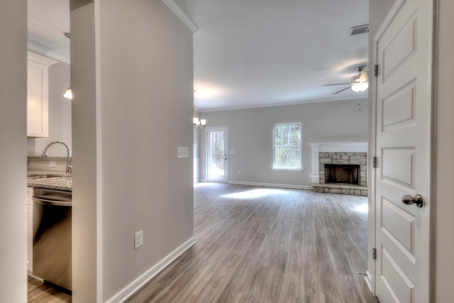 unfurnished living room featuring ceiling fan with notable chandelier, light hardwood / wood-style floors, and a stone fireplace