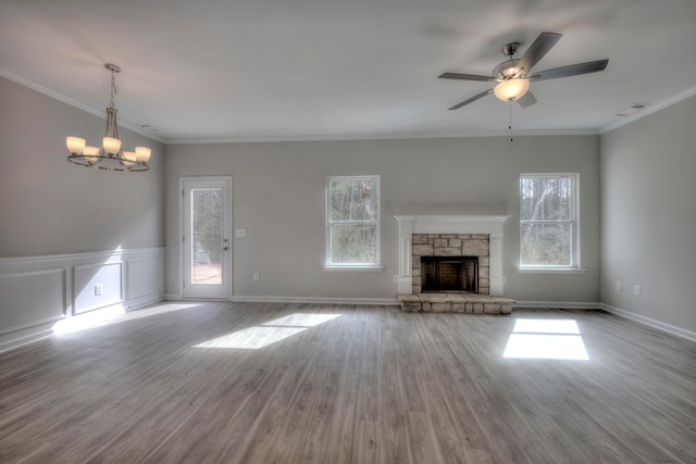 unfurnished living room with ceiling fan with notable chandelier, ornamental molding, a fireplace, and light hardwood / wood-style flooring