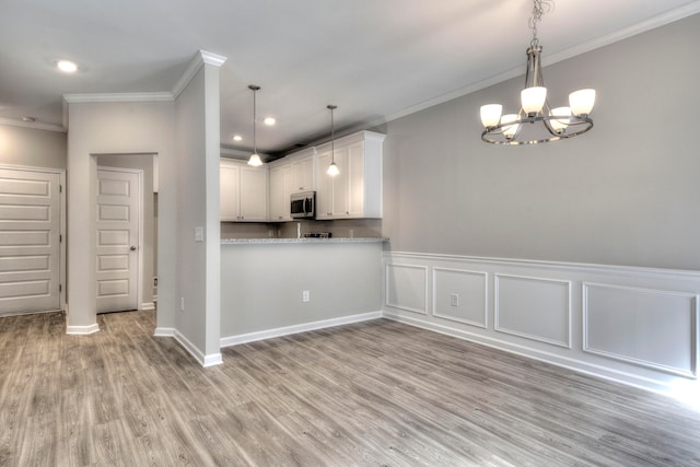 kitchen featuring white cabinets, an inviting chandelier, light wood-type flooring, kitchen peninsula, and ornamental molding