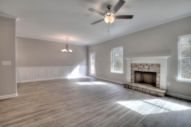 unfurnished living room with a healthy amount of sunlight, ceiling fan with notable chandelier, hardwood / wood-style floors, and a stone fireplace