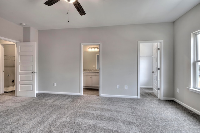 unfurnished bedroom featuring a spacious closet, a closet, light carpet, ensuite bath, and ceiling fan