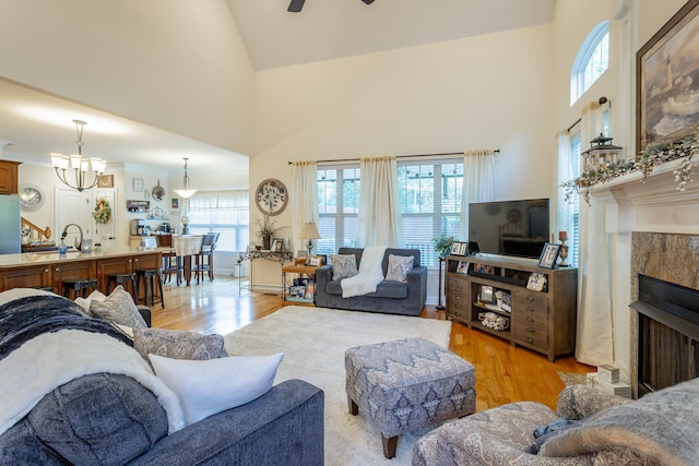 living room with light wood-type flooring, ceiling fan with notable chandelier, high vaulted ceiling, and plenty of natural light