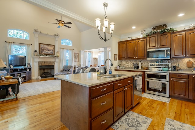 kitchen featuring light wood-type flooring, ceiling fan with notable chandelier, hanging light fixtures, appliances with stainless steel finishes, and a center island with sink