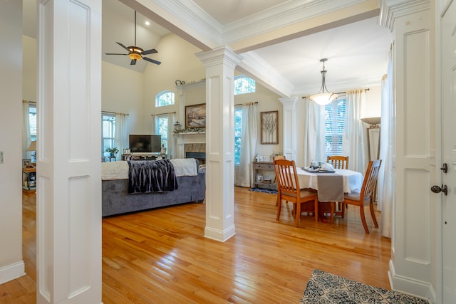 dining area featuring light hardwood / wood-style flooring, ceiling fan, a tiled fireplace, and decorative columns