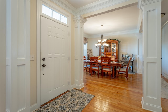 foyer entrance featuring decorative columns, a chandelier, crown molding, and light hardwood / wood-style flooring