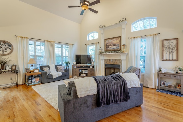 living room with plenty of natural light, ceiling fan, a tiled fireplace, and light wood-type flooring