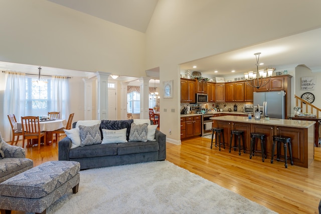 living room featuring high vaulted ceiling, light hardwood / wood-style floors, a chandelier, and ornate columns