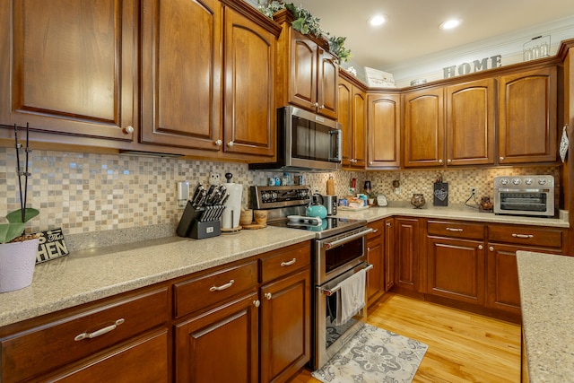 kitchen with stainless steel appliances, light stone counters, decorative backsplash, and light hardwood / wood-style floors