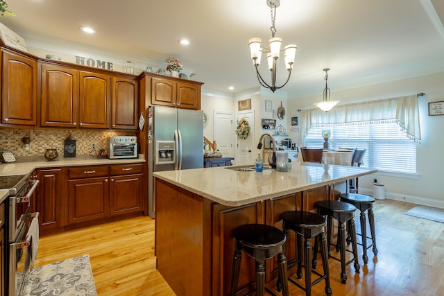 kitchen featuring decorative light fixtures, light hardwood / wood-style flooring, a notable chandelier, an island with sink, and sink