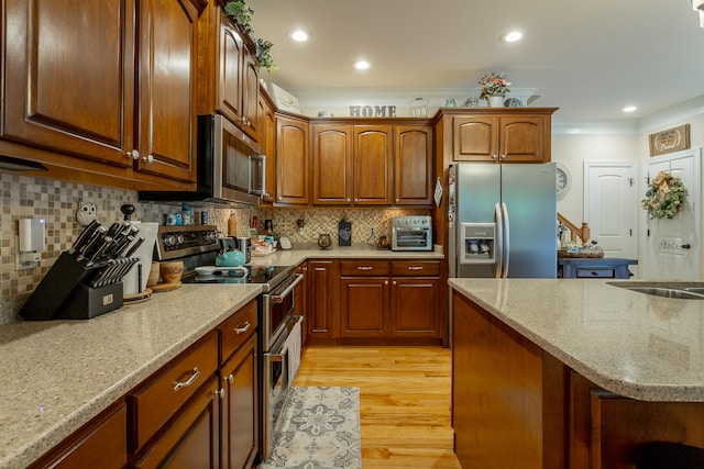 kitchen featuring crown molding, light wood-type flooring, appliances with stainless steel finishes, light stone countertops, and decorative backsplash