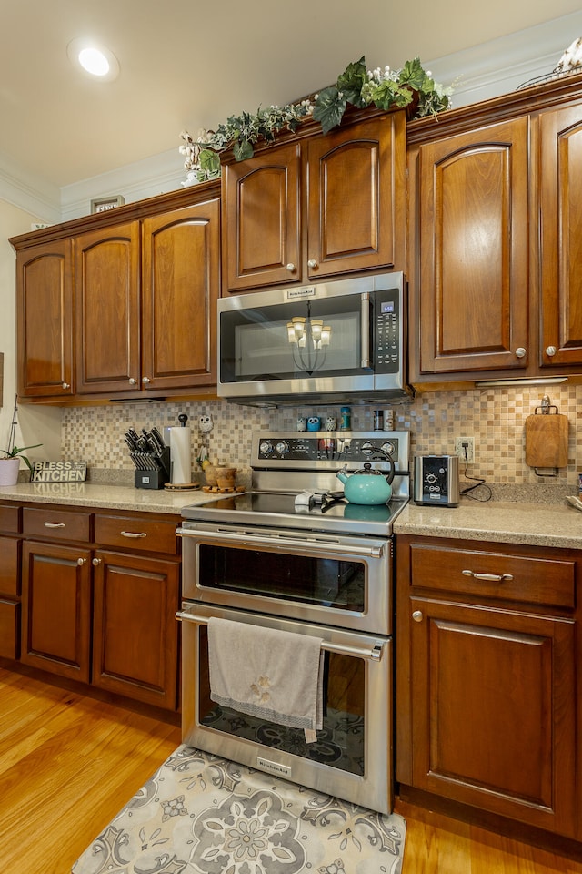 kitchen with crown molding, stainless steel appliances, light hardwood / wood-style flooring, and backsplash