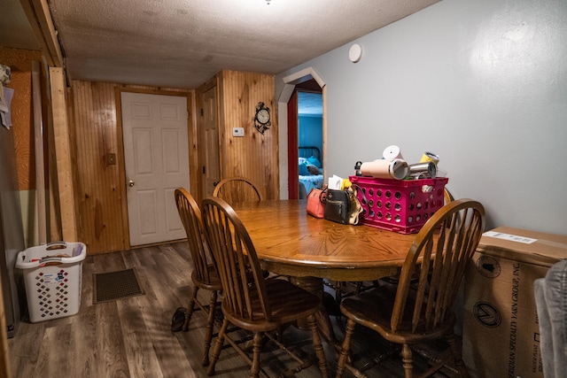 dining area with wooden walls, dark hardwood / wood-style flooring, and a textured ceiling