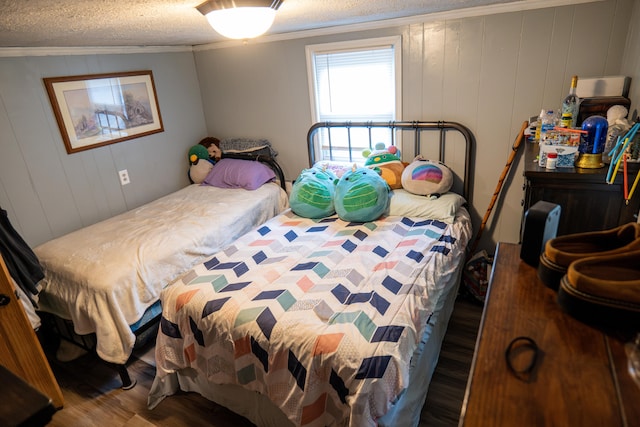 bedroom featuring wood walls, dark hardwood / wood-style floors, ornamental molding, and a textured ceiling