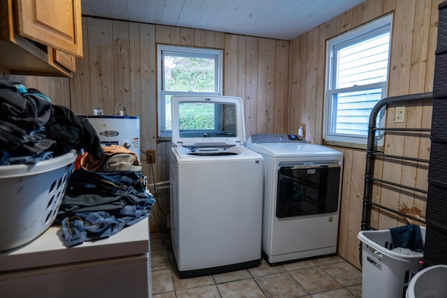 clothes washing area featuring washer and dryer, cabinets, wood walls, and light tile patterned floors