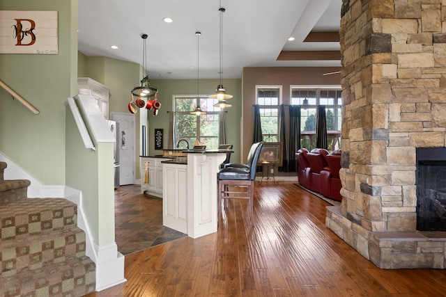 kitchen with white cabinets, dark hardwood / wood-style floors, decorative light fixtures, and a stone fireplace