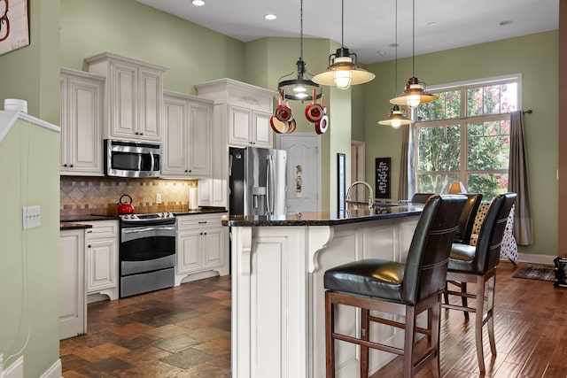 kitchen featuring an island with sink, a kitchen bar, white cabinetry, and appliances with stainless steel finishes