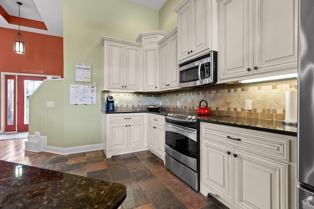 kitchen featuring white cabinets, backsplash, appliances with stainless steel finishes, decorative light fixtures, and dark stone countertops