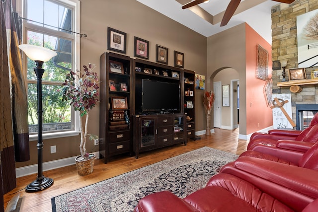 living room featuring a high ceiling, ceiling fan, hardwood / wood-style floors, and a stone fireplace