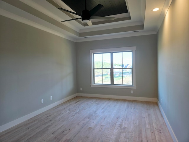 spare room with light wood-type flooring, ceiling fan, a raised ceiling, and ornamental molding