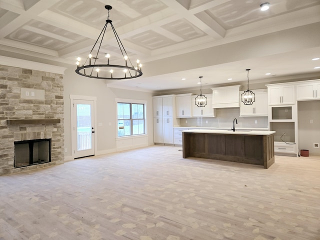 kitchen featuring a stone fireplace, white cabinetry, hanging light fixtures, a kitchen island with sink, and an inviting chandelier