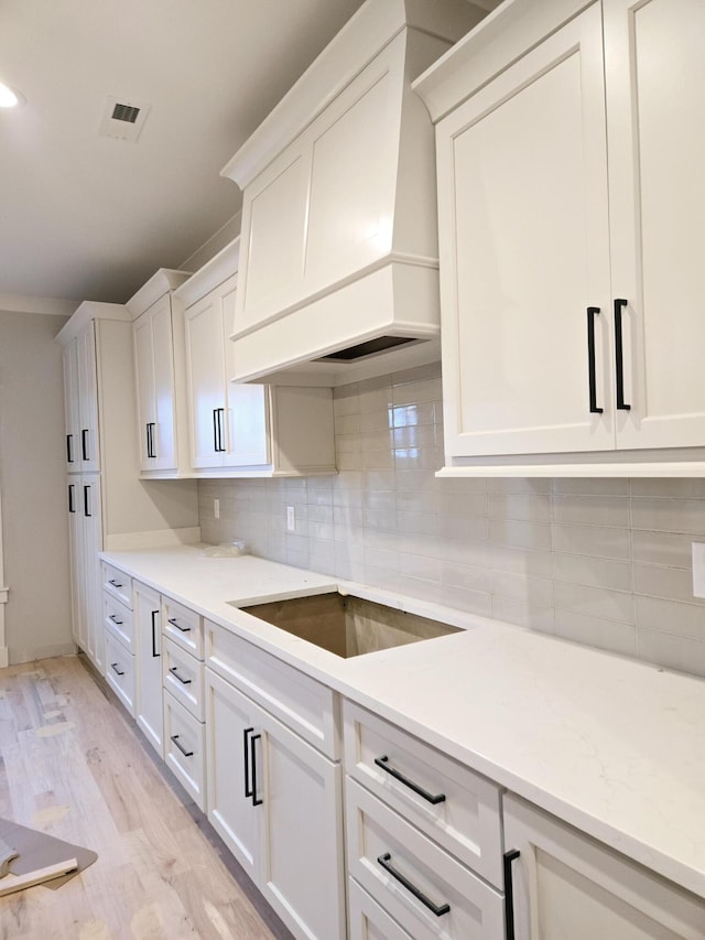 kitchen featuring black electric cooktop, premium range hood, light wood-type flooring, and white cabinets