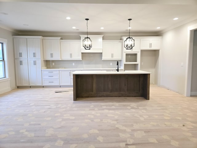 kitchen featuring white cabinets, tasteful backsplash, light hardwood / wood-style floors, hanging light fixtures, and a kitchen island with sink