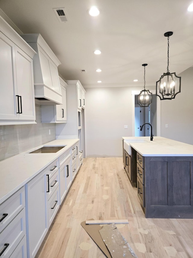 kitchen featuring custom exhaust hood, white cabinets, and decorative light fixtures