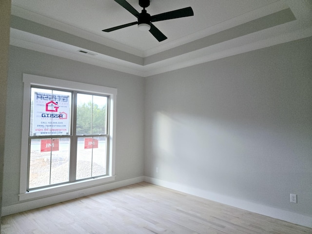 empty room featuring ceiling fan, light hardwood / wood-style flooring, a tray ceiling, and ornamental molding