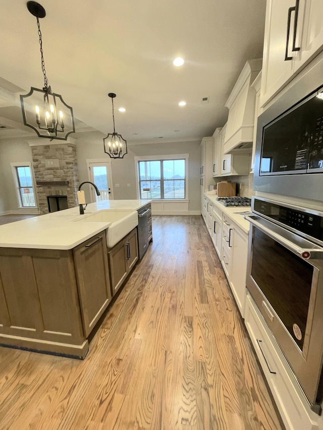 kitchen with a spacious island, white cabinets, sink, hanging light fixtures, and custom range hood