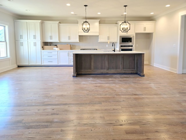 kitchen with appliances with stainless steel finishes, decorative light fixtures, white cabinetry, ornamental molding, and a center island with sink