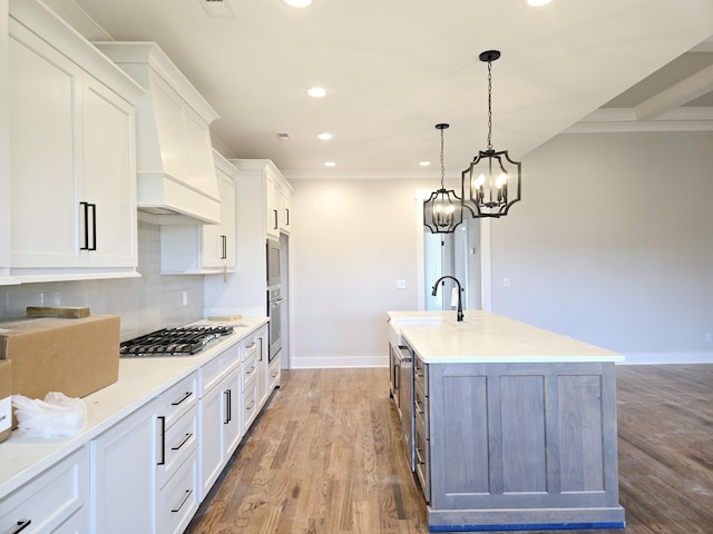 kitchen featuring sink, stainless steel gas stovetop, white cabinets, and a center island with sink