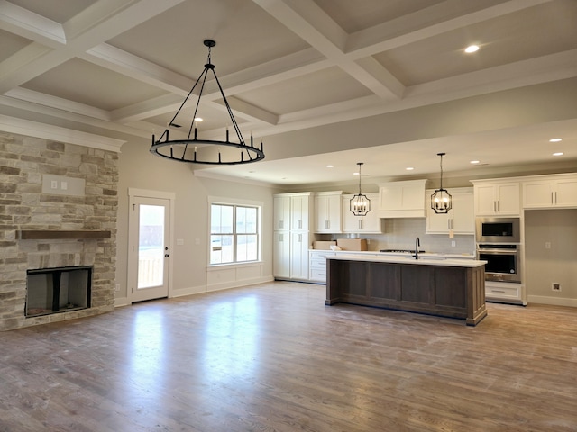 kitchen with white cabinetry, an island with sink, pendant lighting, stainless steel appliances, and light hardwood / wood-style floors