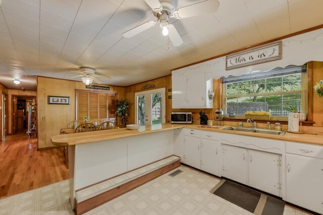 kitchen featuring white cabinets, sink, kitchen peninsula, wood walls, and ceiling fan