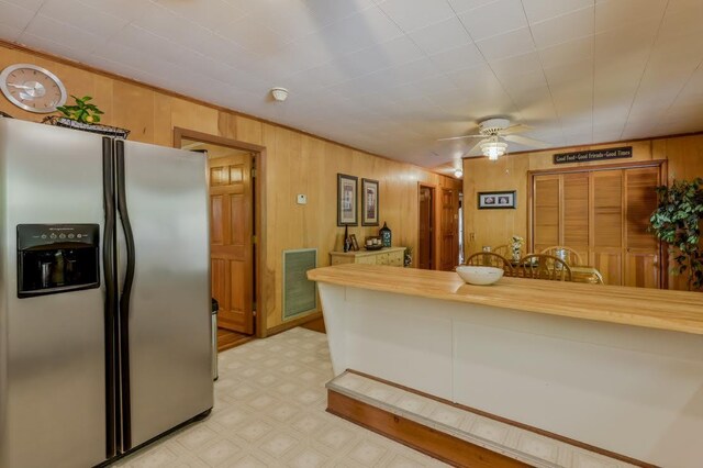 kitchen with stainless steel fridge, butcher block countertops, ceiling fan, and wooden walls