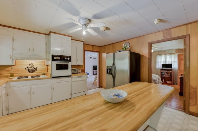 kitchen with white appliances, ceiling fan, ornamental molding, wood walls, and white cabinetry