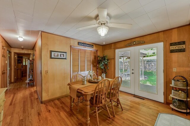 dining room featuring french doors, wood walls, ceiling fan, and light hardwood / wood-style floors