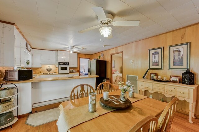 dining space with light hardwood / wood-style flooring, ceiling fan, and wooden walls