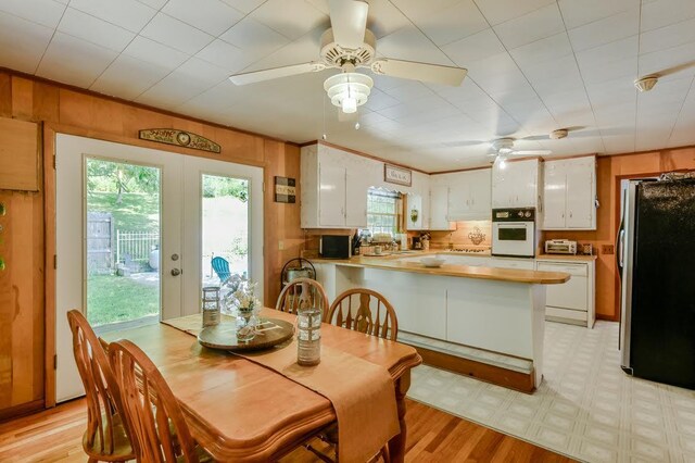 dining area with light wood-type flooring, french doors, wood walls, and ceiling fan