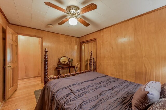 bedroom with ceiling fan, wood walls, a closet, and light hardwood / wood-style floors