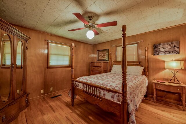 bedroom featuring ceiling fan, wood walls, and light hardwood / wood-style floors