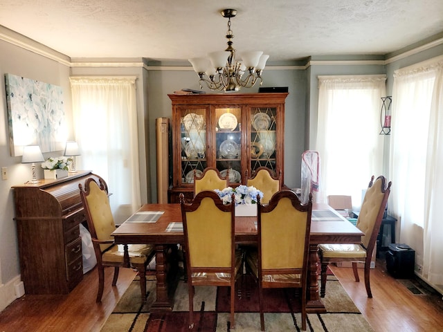 dining area featuring a textured ceiling, wood-type flooring, ornamental molding, and a chandelier