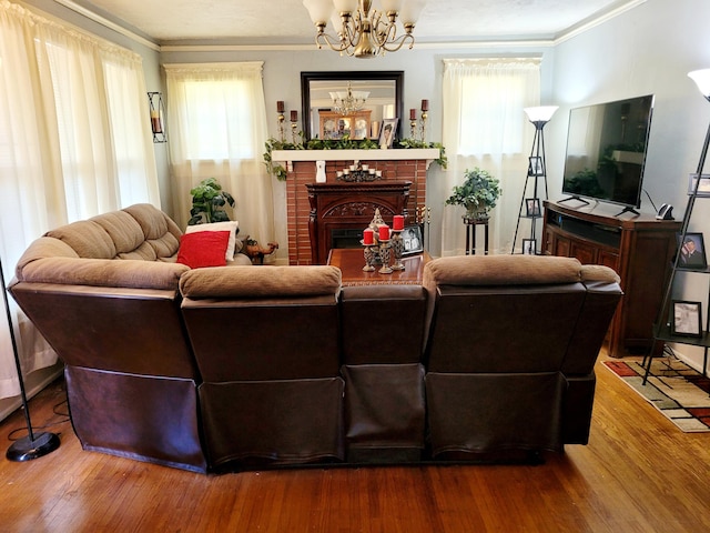 living room with a notable chandelier, hardwood / wood-style flooring, ornamental molding, and a brick fireplace