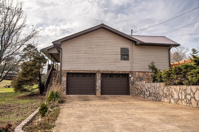 view of side of property with an attached garage, stone siding, driveway, and metal roof