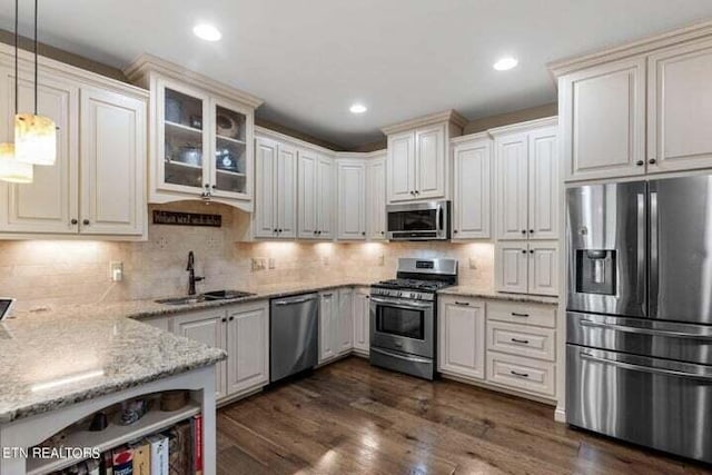 kitchen featuring light stone counters, dark wood-style flooring, a sink, stainless steel appliances, and decorative light fixtures